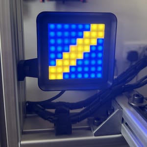 May include: A square LED display module featuring a grid of illuminated pixels. The screen shows a diagonal stripe of bright yellow lights against a background of deep blue lights, all encased within a black frame mounted on a metal rail system.