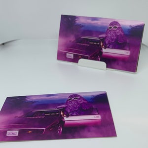 May include: A purple character with sunglasses driving a pink and purple car with the license plate "GRIMACE". The car is driving through a purple and pink landscape with a hazy background.