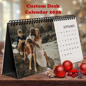 May include: A custom desk calendar for 2026, with a family photograph. The calendar shows September, with red baubles and a star on a wooden surface. The text "Custom Desk Calendar 2026" is displayed at the top.