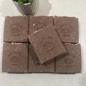 May include: Seven rectangular brown soaps with the text "Charlie's body essentials" and a lotus flower logo. A small white ceramic pot with a green succulent plant is in the background.