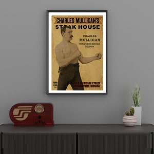 Peut inclure: Une affiche de style vintage annonçant le Steak House de Charles Mulligan. L'affiche présente une photo en noir et blanc de Charles Mulligan, champion de boxe à mains nues, avec le texte "Charles Mulligan's Steak House" et "Charles Mulligan, Champion du monde de boxe à mains nues" en lettres rouges et noires. L'affiche indique également l'adresse "839 S. Meridian Street, Indianapolis, Indiana".