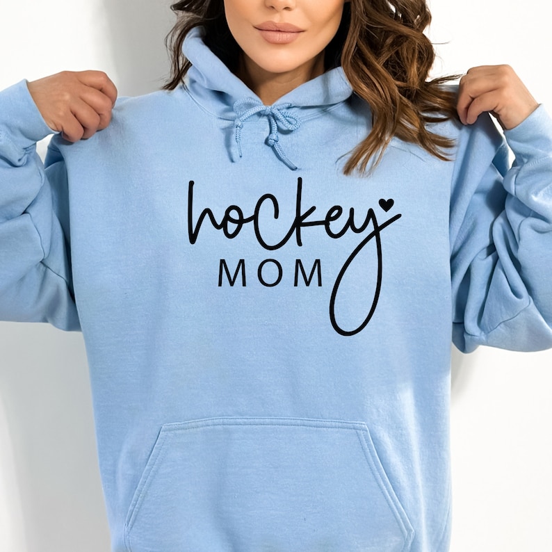 Pu&ograve; includere: Felpa con cappuccio blu chiaro con una grafica nera che dice "hockey mom" con un piccolo cuore.