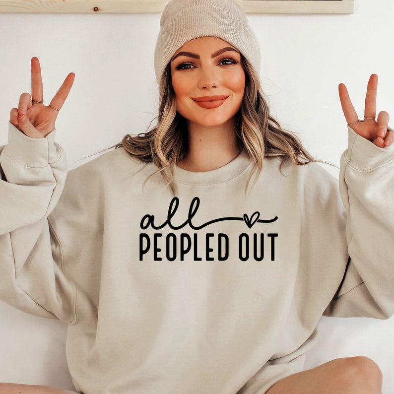 May include: A light beige sweatshirt with the text "all peopled out" in black lettering with a small heart symbol.