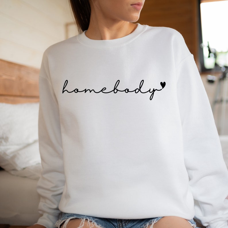 May include: White sweatshirt with the text "homebody" in black cursive lettering with a small black heart to the right of the text.