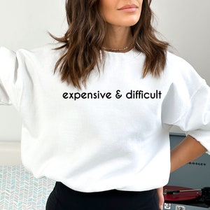 May include: White sweatshirt with the text "expensive & difficult" printed in black.