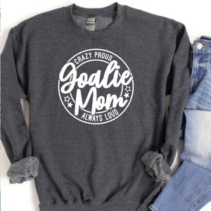K&ouml;nnte beinhalten: Ein dunkelgraues Sweatshirt mit einem wei&szlig;en Kreis-Motiv, auf dem "Crazy Proud Goalie Mom Always Loud" steht.