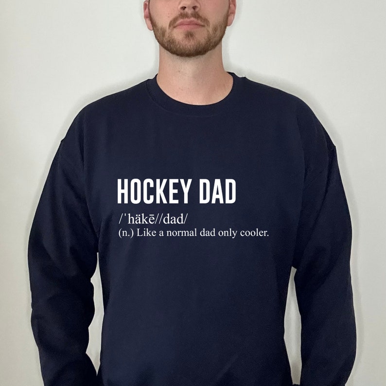 K&ouml;nnte beinhalten: Ein marineblauer Pullover mit dem Aufdruck "HOCKEY DAD /'h&auml;kē//dad/ (n.) Like a normal dad only cooler." in wei&szlig;.