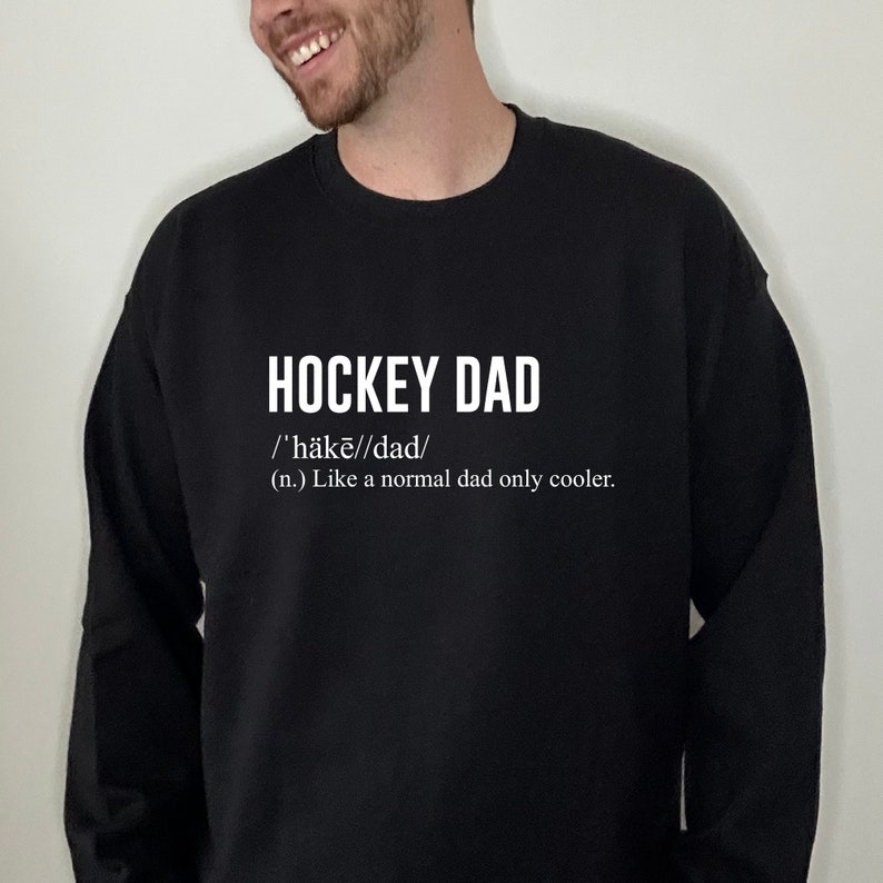 K&ouml;nnte beinhalten: Schwarzer Pullover mit wei&szlig;em Text, der "HOCKEY DAD /'h&auml;kē//dad/ (n.) Like a normal dad only cooler." lautet.