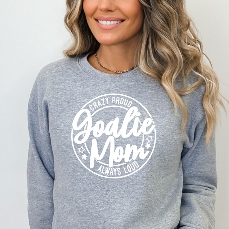 K&ouml;nnte beinhalten: Grauer Pullover mit einem wei&szlig;en Kreis-Motiv, auf dem "Crazy Proud Goalie Mom Always Loud" steht.