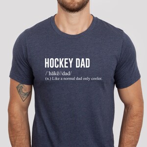 K&ouml;nnte beinhalten: Ein marineblaues T-Shirt mit wei&szlig;em Text, der "HOCKEY DAD /'h&auml;kē//dad/ (n.) Like a normal dad only cooler." lautet.