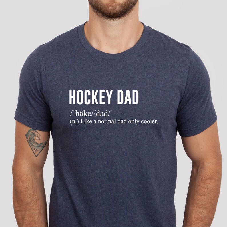 K&ouml;nnte beinhalten: Ein marineblaues T-Shirt mit wei&szlig;em Text, der "HOCKEY DAD /'h&auml;kē//dad/ (n.) Like a normal dad only cooler." lautet.