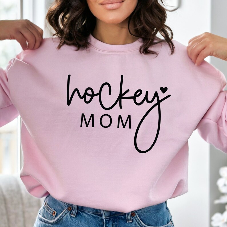 Pu&ograve; includere: Felpa rosa con testo nero che recita "hockey mom" con un piccolo simbolo di cuore dopo "hockey".