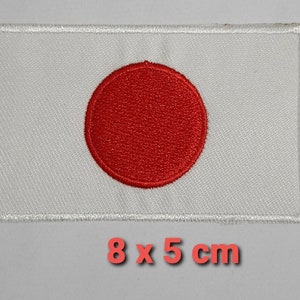 Puede incluir: Parche blanco bordado con un círculo rojo en el centro. El parche mide 8 cm por 5 cm.