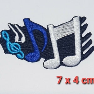Op de afbeelding: Een geborduurde patch met een solsleutel, een blauwe noot en twee witte noten op een zwarte achtergrond. De patch is 7 cm bij 4 cm.