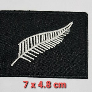 May include: Black fabric patch with a white embroidered silver fern, measuring 7 by 4.8 centimetres.
