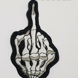 Pode incluir: Um remendo preto bordado com uma mão de esqueleto branca mostrando o dedo do meio. O remendo mede 9,5 x 5,5 cm.