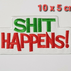 Op de afbeelding: Geborduurde patch, 10 x 5 cm groot, met de tekst "SHIT HAPPENS!" in rode en groene letters op een witte achtergrond. De patch heeft een rechthoekige vorm met een uniek ontwerp aan de bovenkant.