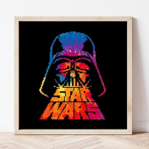 May include: A framed print featuring a pixelated image of Darth Vader's helmet in vibrant colors against a black background. The Star Wars logo is displayed in bold, pixelated text below the helmet.