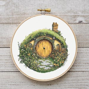 May include: A cross-stitch pattern of a hobbit hole with a round, yellow door and green foliage.