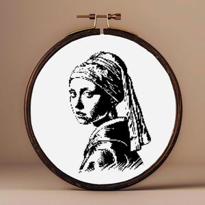 Puede incluir: Aro de bordado en blanco y negro con un diseño de punto de cruz de una mujer con un pañuelo en la cabeza y un gran pendiente de perla.