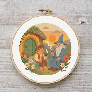 May include: A circular cross-stitch embroidery in a wooden hoop featuring a scene with a small figure in a vest and a bearded figure in a blue robe and pointed hat sitting outside a round green door, with flowers and a sunset background.