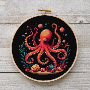 May include: A cross-stitch embroidery hoop with a black background featuring a red octopus with eight tentacles surrounded by coral and seashells.