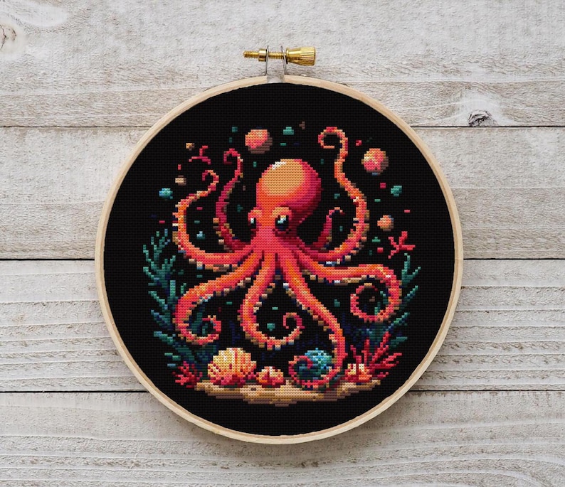 May include: A cross-stitch embroidery hoop with a black background featuring a red octopus with eight tentacles surrounded by coral and seashells.