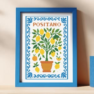 Puede incluir: Una obra de arte en punto de cruz enmarcada que representa un limonero en una maceta de terracota. La obra tiene un marco azul y la palabra "POSITANO". El fondo es blanco con un borde azul.