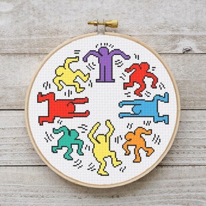 Könnte beinhalten: Ein runder Stickrahmen mit einem weißen Stoff, der ein farbenfrohes Design aus acht tanzenden Strichmännchen in einem Kreis zeigt. Die Figuren sind in verschiedenen Schattierungen von Rot, Orange, Gelb, Grün, Blau, Lila und Rosa.