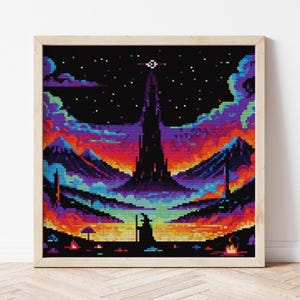 May include: A framed cross-stitch depicting a pixelated fantasy landscape. The scene features a dark tower, mountains, and a figure in silhouette against a vibrant sky of purple, orange, and blue hues. The artwork is framed in a light wood.