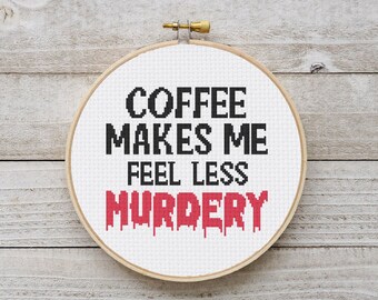 Può includere: Un telaio da ricamo a punto croce con la scritta "COFFEE MAKES ME FEEL LESS MURDERY" in nero e rosso. Il testo è centrato su uno sfondo di tessuto bianco, incorniciato da un cerchio di legno.