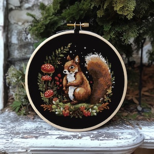 May include: A cross-stitch embroidery hoop with a black fabric background featuring a brown squirrel surrounded by red mushrooms, green leaves, and berries.