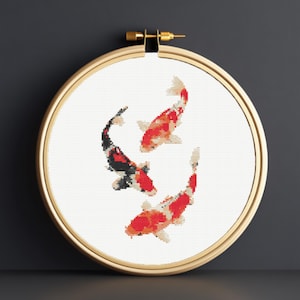 May include: A cross-stitch embroidery hoop featuring three koi fish in red, black, and white. The fish are arranged in a circular pattern against a white background, framed by a wooden hoop.