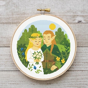 May include: A cross-stitch embroidery in a wooden hoop depicts a couple in an outdoor scene. The woman wears a white dress and holds a bouquet. The man wears green clothing. The background features green trees, blue sky, and a yellow sun.