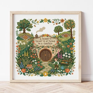 Op de afbeelding: Ingelijste kruissteekkunst met een hobbit-huis met een ronde deur en tuin. De tekst luidt: "A hobbit's heart is at home in a garden." De scène toont bomen, bloemen en een hobbit-personage, allemaal in een gedetailleerd, kleurrijk ontwerp.