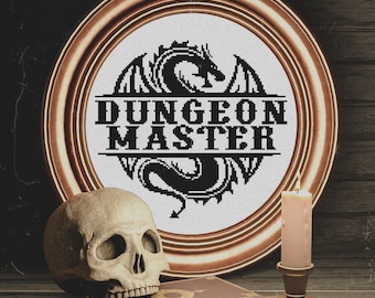 May include: A framed cross-stitch design featuring a black dragon with the text "Dungeon Master" in a white circle. The frame is a copper color and is sitting on a wooden table with a skull and a candle.