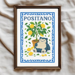 May include: Cross-stitch artwork in a wooden frame. The design features a lemon tree, the word "POSITANO", and a blue and white character. Yellow lemons and green leaves are visible.