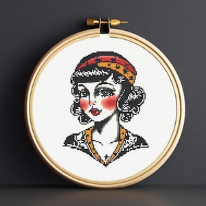 Peut inclure: Un motif de point de croix représentant une femme aux cheveux noirs portant un foulard rouge et jaune. La femme a un tatouage noir et blanc sur le bras.