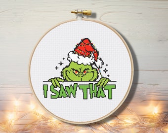 May include: Green Grinch character wearing a red Santa hat with white trim and lights. The Grinch is peeking over a white sign with the text "I SAW THAT" in green letters.