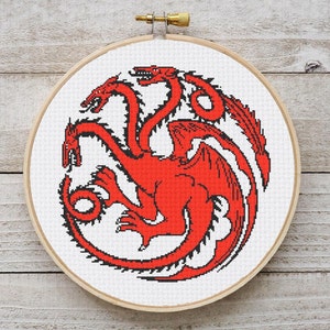 Op de afbeelding: Rood kruissteekpatroon met een driekoppige draak in een ronde borduurring. De draak is om zichzelf gekruld met zijn vleugels uitgespreid.