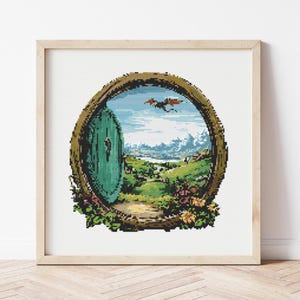 May include: A square cross-stitch pattern framed in light wood, featuring a circular green door set into a brown wooden frame. The scene depicts a rolling green landscape with distant blue mountains, a bright sky, and a small flying creature.