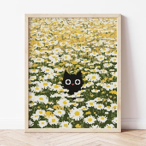 May include: Cross-stitch art print of a black cat peeking out from a field of white and yellow daisies. The artwork is framed in a light wood frame and set against a white wall. The daisies are in full bloom, creating a vibrant and cheerful scene.