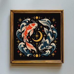 May include: A square cross-stitch embroidery in a gold frame featuring two koi fish swimming in a circle against a black background. One fish is white and orange, the other is white and dark blue. The design includes stylized waves, a yellow crescent moon, and small stars.