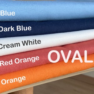 Op de afbeelding: Een stapel stofstalen in verschillende kleuren, waaronder blauw, donkerblauw, crèmewit, roodoranje en oranje. Het woord "OVAL" staat in wit op het roodoranje staal.