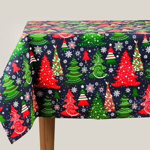 Pode incluir: Uma toalha de mesa azul com um padrão de árvore de Natal. As árvores são vermelhas, verdes e brancas com flocos de neve sobre um fundo azul escuro.