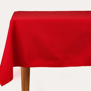 Può includere: Una tovaglia rossa unita drappeggiata su un tavolo di legno. La tovaglia è liscia e ha una leggera lucentezza.