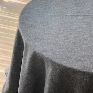 May include: A round, dark grey tablecloth with a textured weave. The tablecloth is made of linen and has a subtle sheen. The tablecloth is shown on a wooden floor. Anthracite.