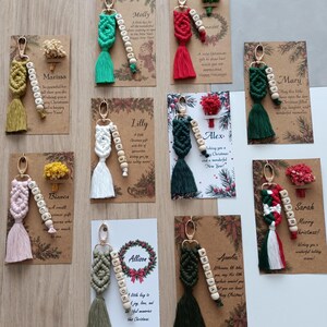 Personalized Christmas macrame keychain handmade with soft cotton cord, wooden name beads, a tassel, and your choice of metal hook. Customize the colors and name to create a meaningful holiday gift for friends, best friends, classmates, or loved ones. Add a custom Christmas card or dried flowers for a more complete presentation. A thoughtful choice for stocking stuffers, Secret Santa gifts, holiday exchanges, and small personalized Christmas presents.