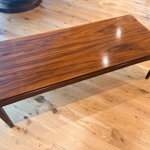 May include: A rectangular coffee table featuring a polished, dark brown wood grain surface with visible natural patterns. The table has a smooth, glossy finish and is supported by four straight, tapered legs that extend from the corners.