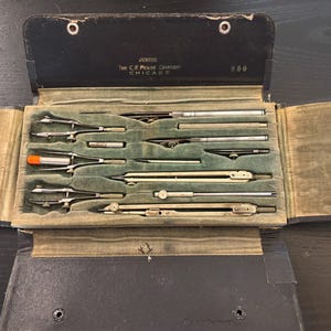 Peut inclure: Un ensemble d'instruments de dessin vintage dans un étui pliant noir avec un intérieur en velours vert. Le set comprend divers compas, diviseurs et rallonges en métal. L'étui porte l'inscription JUNIOR, The C.F. Pease Company, CHICAGO, 800.